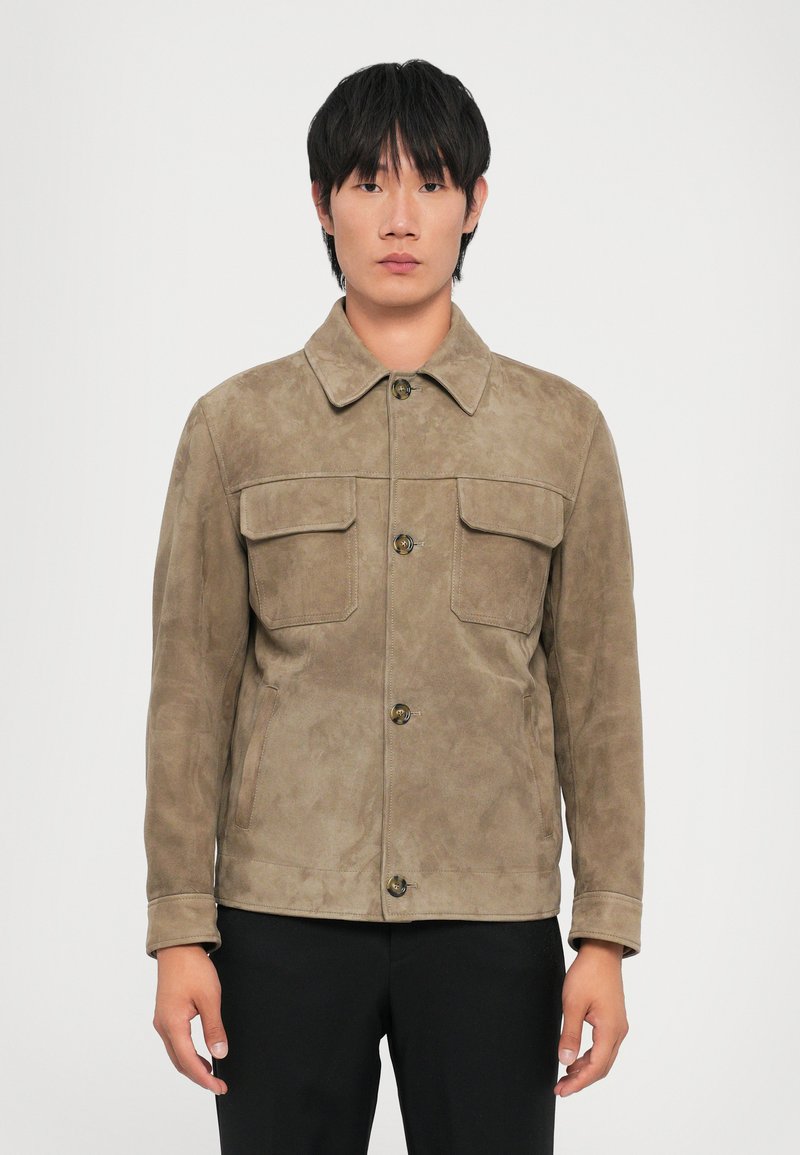 Brown suede jacket with a collared neck, two front pockets, button closure, and long sleeves, worn by a model against a white background.
