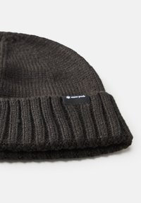 Dark gray knitted beanie with a ribbed texture, featuring a black label with white text. The fabric appears thick and warm.