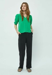 Blusa verde con scollatura a V e maniche a sbuffo, abbinata a pantaloni neri a gamba larga. La texture appare liscia; il design della blusa è morbido.