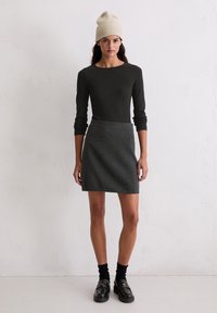 Zwarte langetermijn top, grijze mini rok, crèmekleurige gebreide beanie, zwarte sokken en instappers. Eenvoudige snit en textuur materialen.