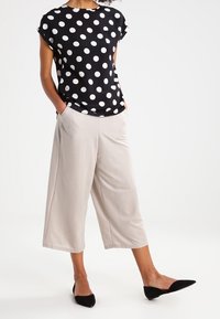 Černý top s krátkým rukávem a bílými puntíky v kombinaci se světle béžovými culotami. Outfit doplňují špičaté černé balerínky.