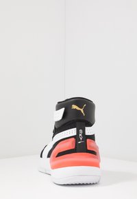 Bottines Puma noires, blanches et rouges vues de l'arrière, montrant le logo Puma doré et le texte "SKY" sur l'onglet du talon.