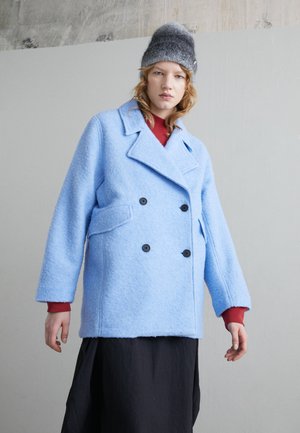 Διπλής όψης παλτό από υφασμάτινο λείο μπλε μαλλί, με μαύρα κουμπιά, λαιμόκοψη κανονικού μήκους και πλαινές τσέπες, συνδυασμένο με κόκκινη μπλούζα.