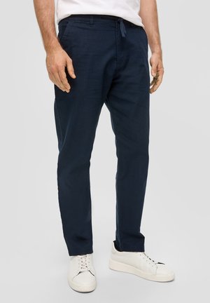 Pantalons tapereds bleu marine avec taille élastique et cordon de serrage, fabriqués en tissu léger, associés à des baskets blanches.