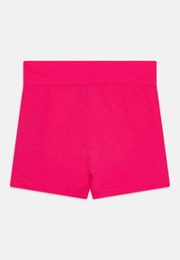 Shorts en coton rose avec une taille élastique, présentant une texture lisse et un design simple, sans embellissements. Pas de poches ni de motifs visibles.