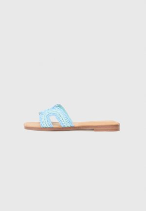 Lichtblauwe geweven slip-on sandaal met een platte houten zool, voorzien van een openteen en twee kruislings bevestigde banden. Textuurmateriaal voegt visuele interesse toe.