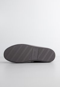 Suela de un zapato gris oscuro con un patrón de huellas circulares y una sección rectangular con el nombre de la marca "JOOP!" en relieve.