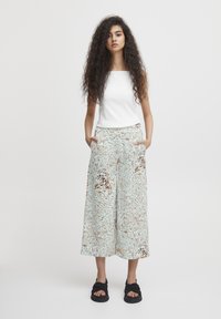 Haut sans manches blanc à côtes ; pantalon large à motifs bleu clair avec des accents marron et orange ; sandales noires à bretelles épaisses.