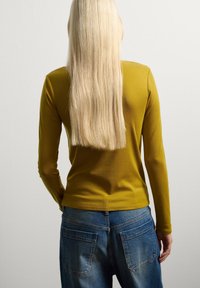 Langsleeve mosterdgele top met een strakke pasvorm, gecombineerd met blauwe denim jeans met achterzakken en een relaxte pasvorm.