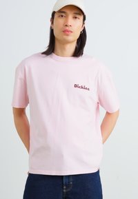 Light pink cotton t-shirt featuring a brown "Dickies" logo on the left chest, short sleeves, and a relaxed fit.