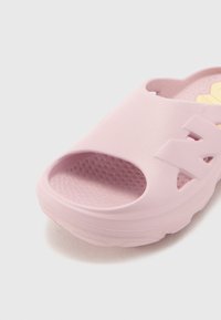 Roza slip-on sandal z odprtim prstom, izdelana iz teksturirane gume, z perforiranim podplatom in izrezljanim dizajnom za ventilacijo.