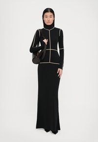 Black long-sleeve dress with a fitted silhouette, featuring cream lines forming a geometric pattern. Worn with a round black bag.