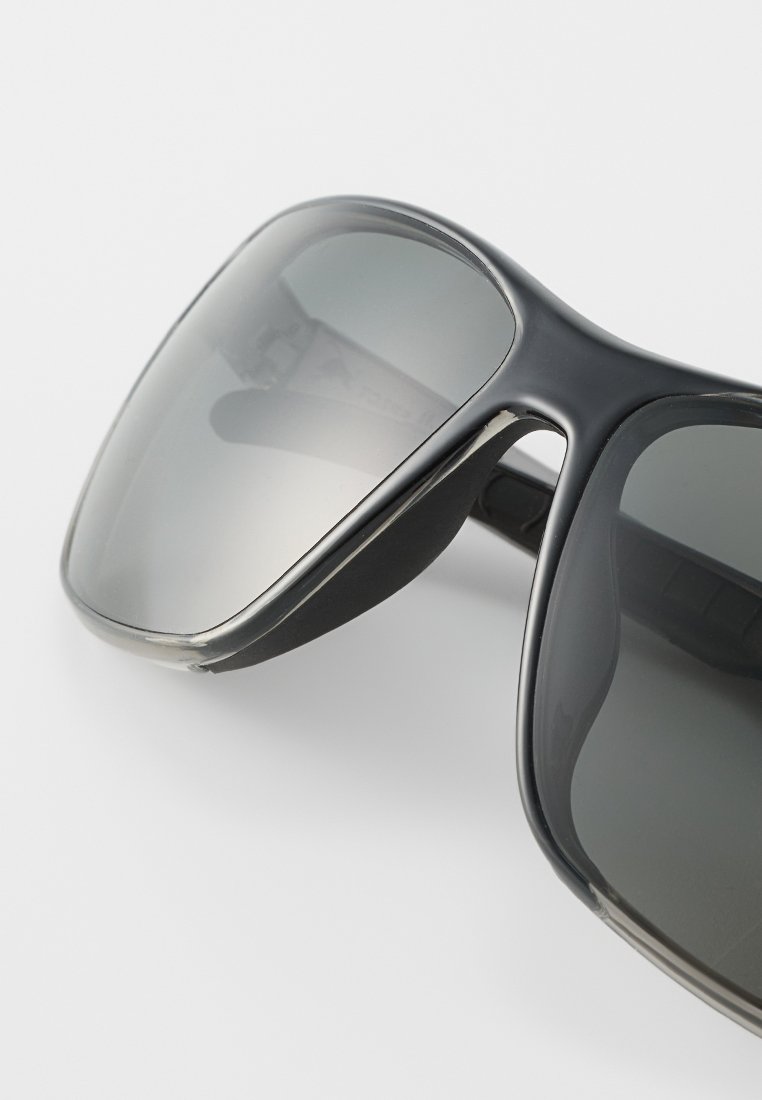 Czarne okulary przeciwsłoneczne z szerokimi, zakrzywionymi oprawkami, szarymi soczewkami i gumowymi akcentami w okolicach skroni, o gładkim, błyszczącym wykończeniu.
