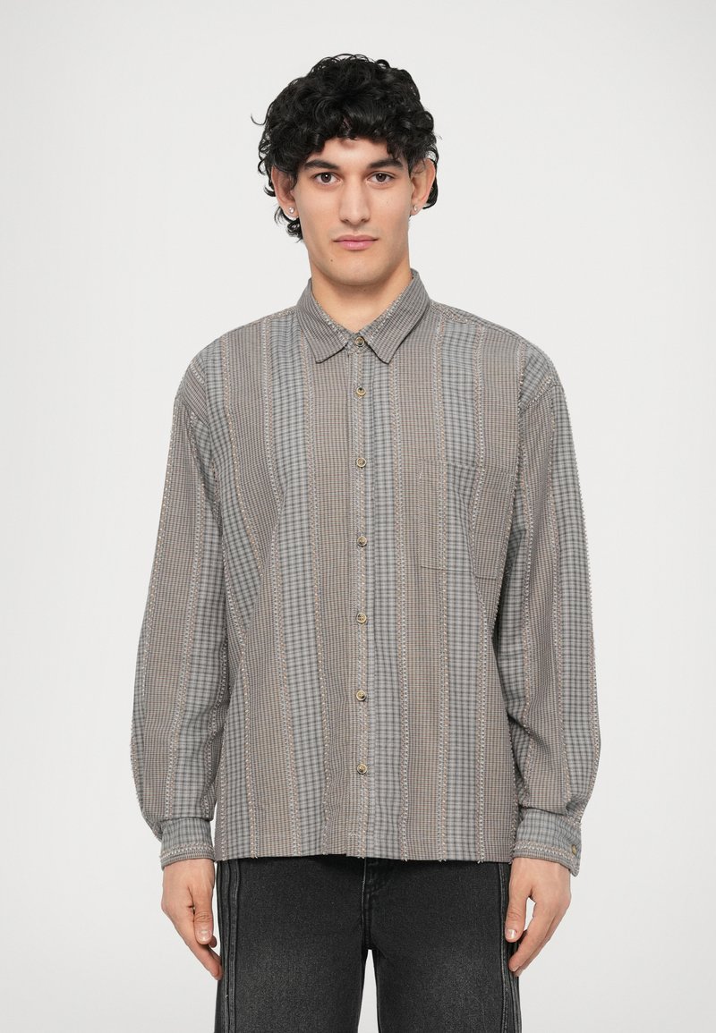 Camicia button-up grigia con motivo a quadri, caratterizzata da maniche lunghe, colletto e taschino sul petto. Texture morbida con dettagli sottili.