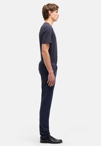 Maglietta e pantaloni blu navy con vestibilità aderente, materiale in cotone e tessuto liscio. Scarpe eleganti nere completano l'outfit. Modello visto di profilo.