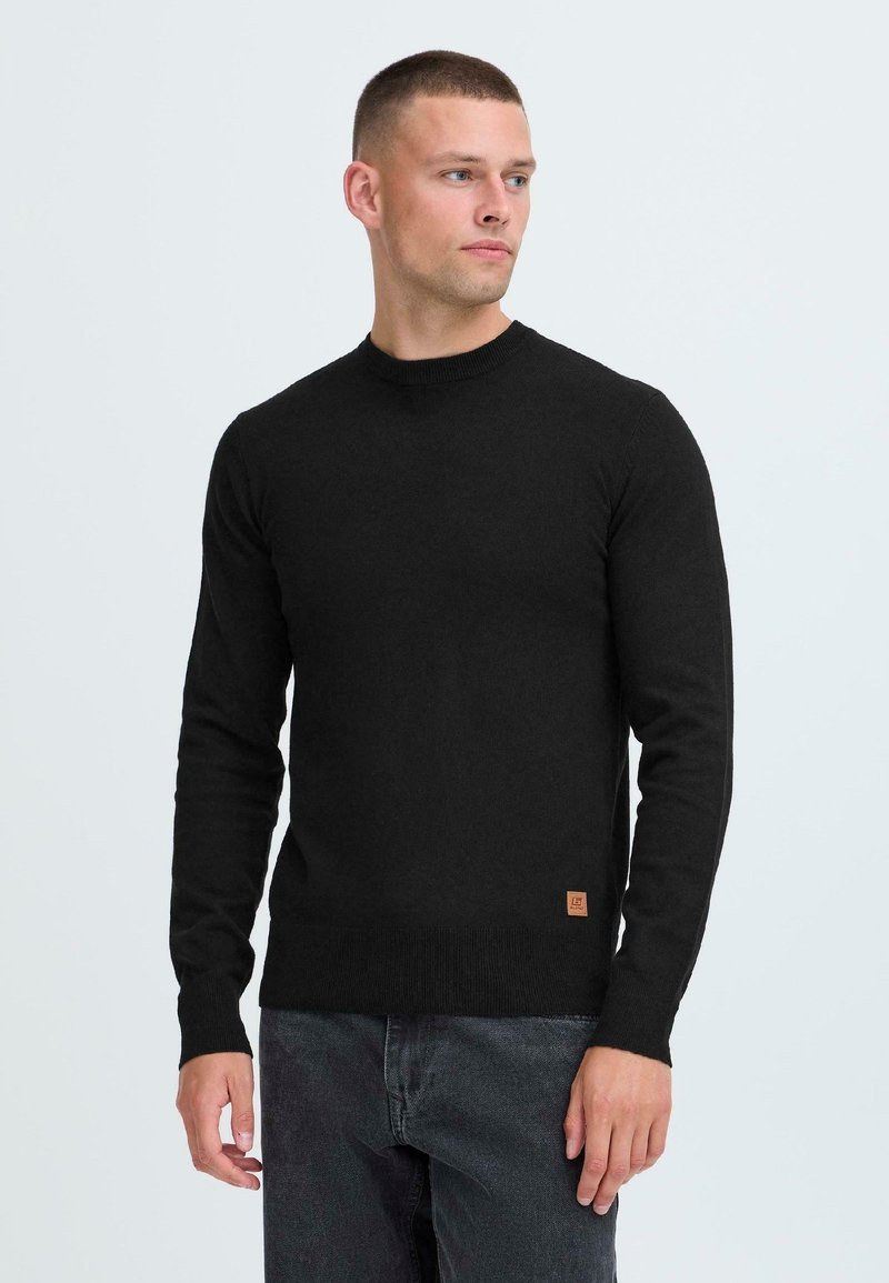 Zwarte trui met een ronde halslijn en lange mouwen. Gemaakt van een zachte stof, met ribbelmanchetten en een klein merkembleem aan de onderzoom.