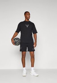 Svart treningsantrekk med kortermet t-skjorte og shorts, begge med en okse-logo. Inkluderer en basketball og hvite joggesko.