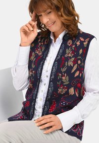 Navy gebreide vest met bloemen- en paisleyontwerpen in rood, groen en blauw. Met een hoge halslijn en een open voorkant.