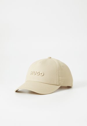 Beige baseball cap with a curved brim and embroidered "HUGO" logo on the front. Made of durable fabric, featuring a structured design.
