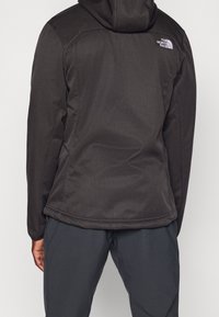 Giacca nera con cappuccio realizzata in un tessuto leggero e durevole; presenta una texture liscia con pannelli delle spalle a contrasto e un dettaglio del logo sul retro.