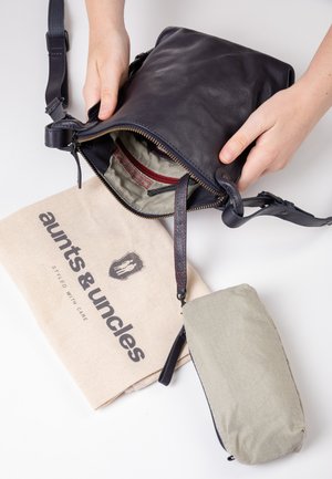 Small navy leather bag with a zipper, showcasing a striped interior and red accent. Includes a beige cotton bag with printed logo.