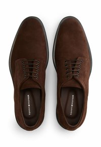 Zapatos de ante marrón con cordones negros, punta redondeada y superficie texturizada. Presentan una suela de caucho negra y un interior de marca.