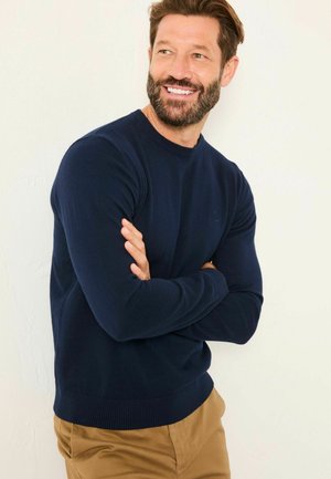Navy blue knit sweater with a crew neckline and ribbed cuffs and hem; smooth texture with a fitted silhouette. Pants are khaki.