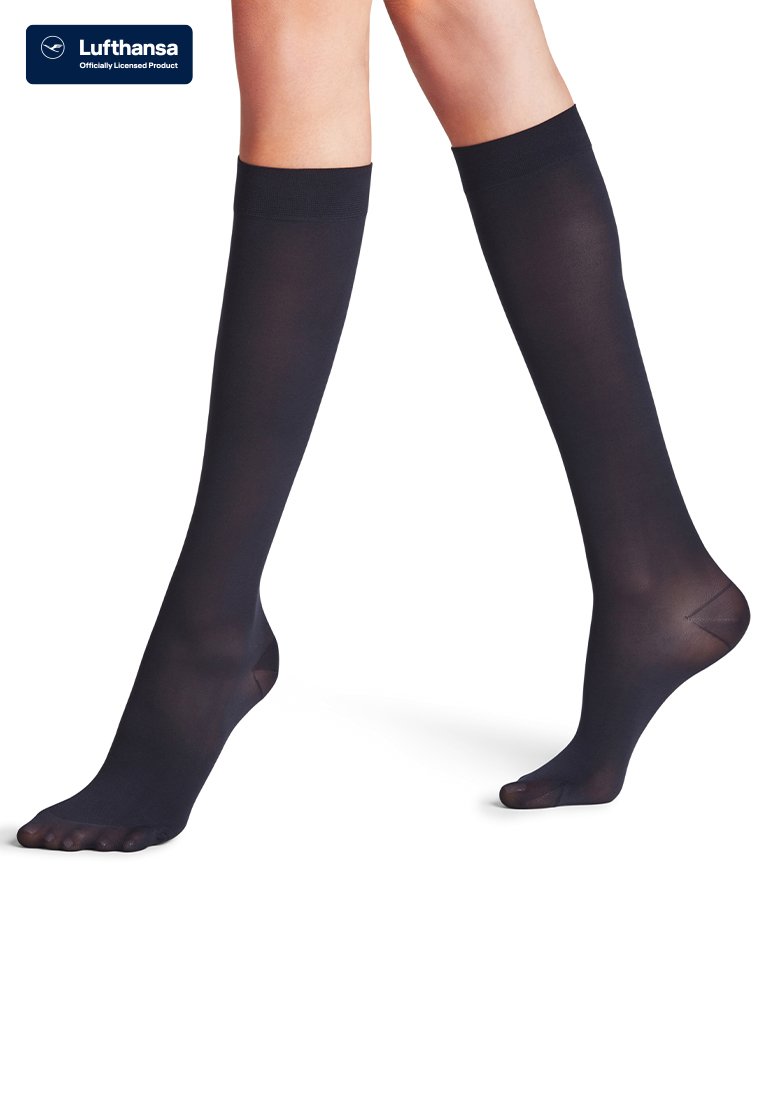 Jambes portant des chaussettes noires à bouts ouverts montant jusqu'aux genoux, un pied légèrement levé, fond blanc uni, logo Lufthansa dans le coin.