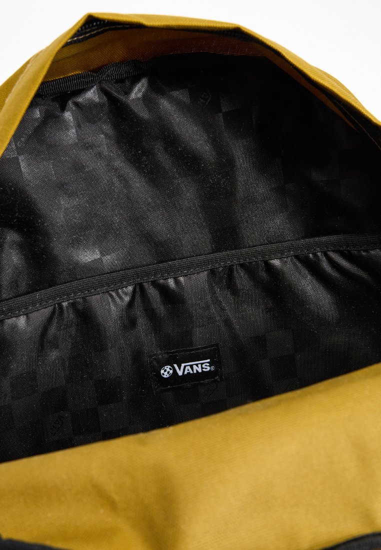 Interior negro de una mochila con tela exterior amarilla. Presenta un logo negro de Vans y un compartimento con tela recogida para almacenamiento.