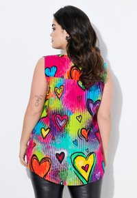 Top senza maniche in tessuto multicolore caratterizzato da un vivace motivo a cuori. I colori dello sfondo includono rosa, blu, verde e viola. Orlo arrotondato.