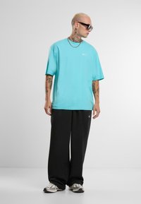 Turquoise oversized T-shirt met logo, gecombineerd met zwarte losse broek en grijze sneakers, met een soepele textuur en een relaxte pasvorm.