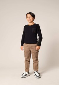 Zwarte longsleeve shirt met een borstzak, gecombineerd met beige cargobroeken en zwart-witte sneakers. Neutrale achtergrond.