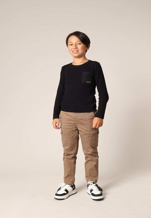 Zwarte longsleeve shirt met een borstzak, gecombineerd met beige cargobroeken en zwart-witte sneakers. Neutrale achtergrond.