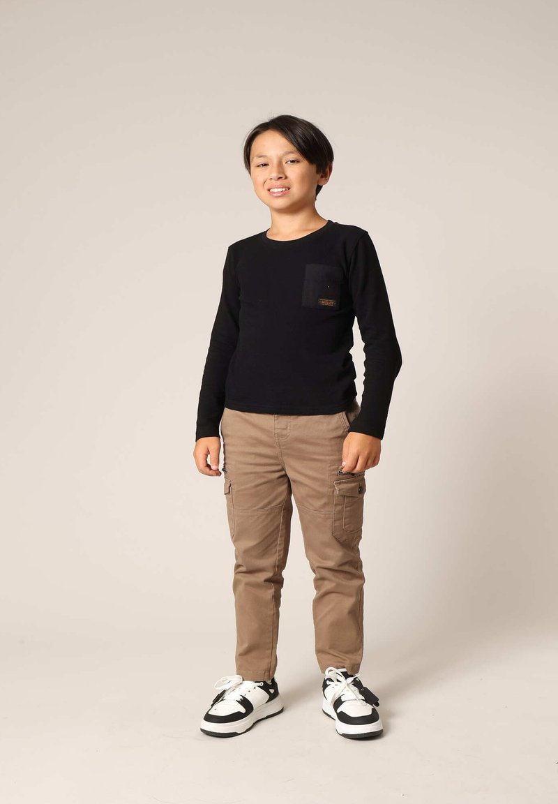 Zwarte longsleeve shirt met een borstzak, gecombineerd met beige cargobroeken en zwart-witte sneakers. Neutrale achtergrond.