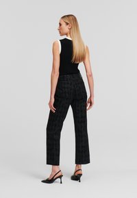 Juodos raštuotos aukšto juosmens kelnes su tiesiomis klešnėmis, derinamos su juodu tank topu, kuris turi baltus apdailos elementus, ir juodais slingback kulnais.