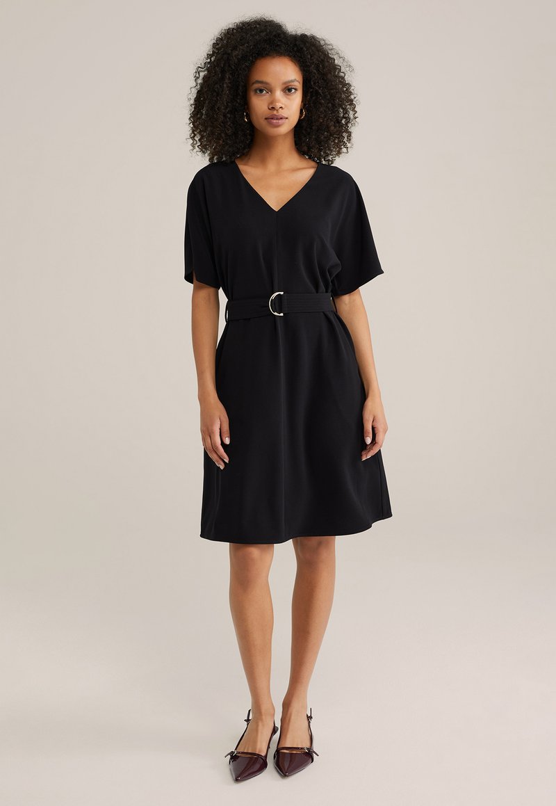 Robe noire à col en V avec des manches courtes et une ceinture à la taille dotée d'une boucle ronde. Tissu lisse avec une coupe décontractée et une longueur au genou.
