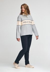 Szary longsleeve polo z kremowym poziomym paskiem i napisem "POLO CLUB". Połączony z ciemnymi spodniami i jasnymi tenisówkami. Gładka tekstura.