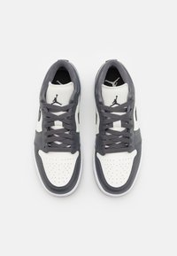 Paire de baskets basses blanches et gris foncé avec logo Jumpman noir sur la languette, vue de dessus sur un fond uni.