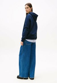 Felpa con cappuccio blu navy dal fit rilassato, abbinata a jeans in denim leggero a gamba larga blu chiaro. Texture liscia, design casual e accenti minimali.