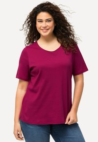 Magenta kortærmet t-shirt lavet af blødt stof, med en rund halsudskæring og en afslappet pasform, parret med mørkeblå jeans.