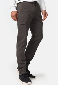 Dark gray cargo pants with side pockets, straight-leg fit, made of cotton-blend fabric, paired with black sneakers.