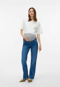 Graviditetsoutfit med en hvid cropped top og blå denim straight-leg jeans, samt et gråt mavebånd for støtte. Brune flade sko.
