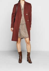 Viininpunainen villasekoitteinen takki, jossa on tuplapainikkeet, päällä vaaleanbeige eläinkuosinen mekko. Ruskeat tekstuuri nilkkurit täydentävät asun.