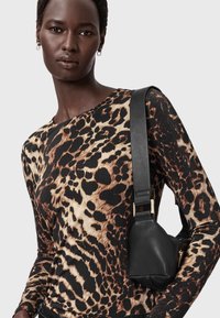 Lauvas raksta garām piedurknēm tops siltos toņos ar pieguļošu siluetu; apvienots ar mazu melnu ādas somu ar biezu siksnu un zelta aparatūru.