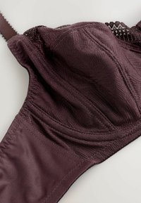Reggiseno in pizzo viola scuro con ferretto e spallina regolabile, che mostra la trama dettagliata del tessuto e le cuciture su una superficie chiara.
