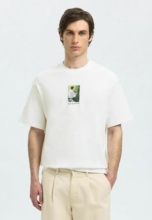 Hvid bomulds t-shirt med korte ærmer, der har et rektangulært grafik, der viser en person omgivet af grønt. Løst fit.