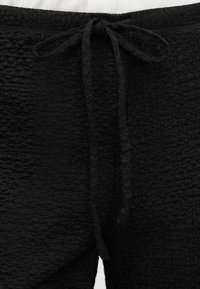 Μαύρο σορτς από υφασμάτινη ύφανση με ελαστική μέση και δεμένη κορδονίτσα στο μπροστινό κέντρο.