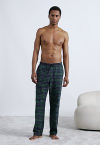 Grønne og blåternet loungebukser med elastik i taljen og snøre, lavet af blødt stof, vist på en model med bar overkrop.