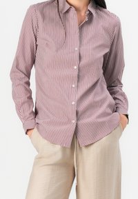 Długi rękaw w czerwono-białe paski z kołnierzykiem, z przodem zapinanym na guziki i luźnym krojem. Noszony z beżowymi spodniami.