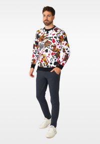 Maglione colorato con motivi di carte da gioco in rosso, nero e bianco. Polsini e vita a coste neri. Abbinato a pantaloni scuri e strutturati e sneakers bianche.